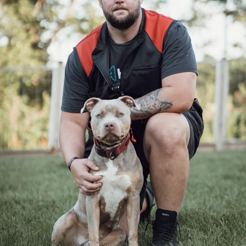Zack kneeling with a pit bull he trained