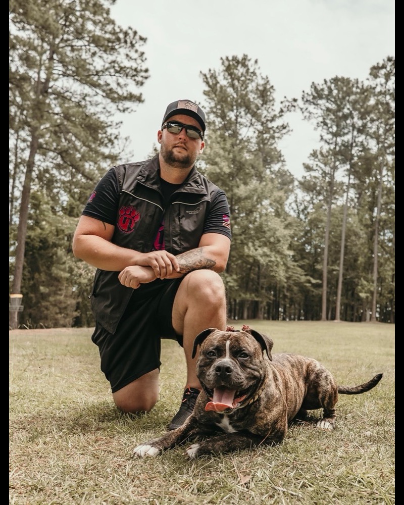 Zack kneeling with a calm, confident dog he trained